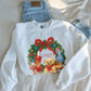 White sweatshirt with Christmas design featuring a wreath, teddy bear, and presents on a white background.