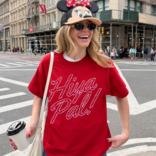 Person wearing a red 'Hiya Pal!' t-shirt and Minnie Mouse hat on a city street.